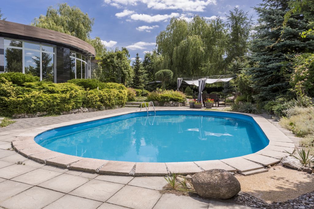 Oval swimming pool in big garden next to modern villa